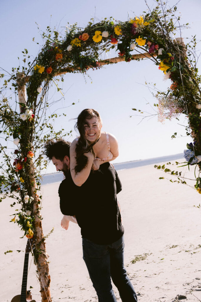 floral archway on beach spring colors with couple under archway on folly beach sc charleston documentary wedding photographer