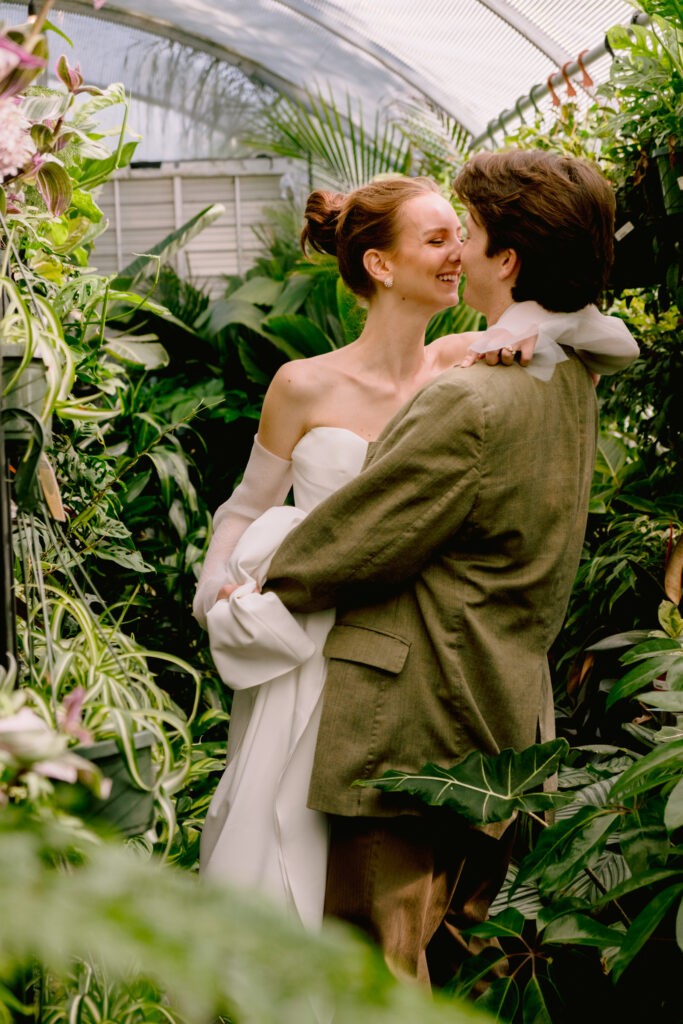 bride and groom in greenery at greenhouse styled shoot wearing lovely bride