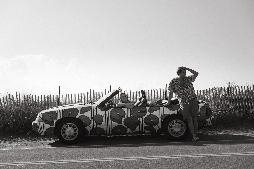 black and white image of couple posed in car on beach documentary wedding and engagement photography