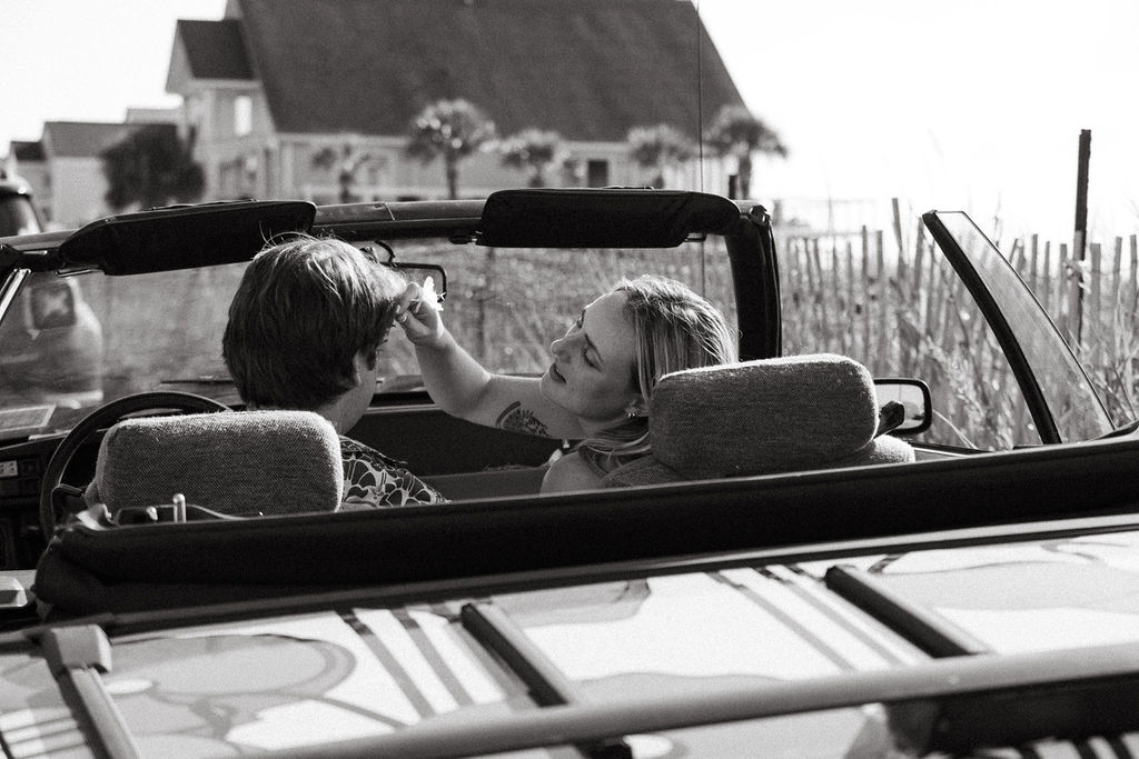 black and white image of engagement couple in car on beach