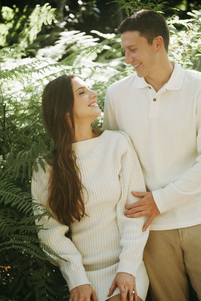 couple in all white with greenery ferms in trees documentary style engagement shoot hampton park engagement photoshoot