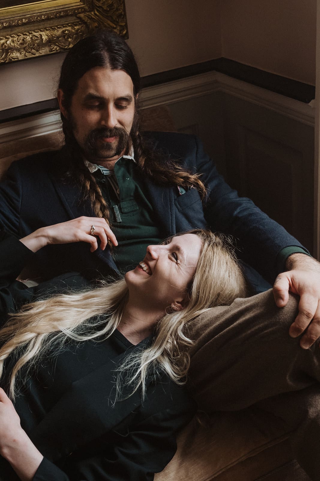 couple laying on couch for engagement shoot, moody and dark