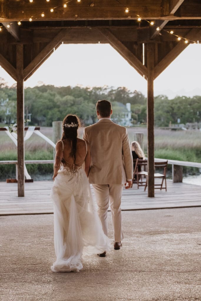 bride and groom walking at cotton dock at boone hall plantation at sunset with twinkle lights