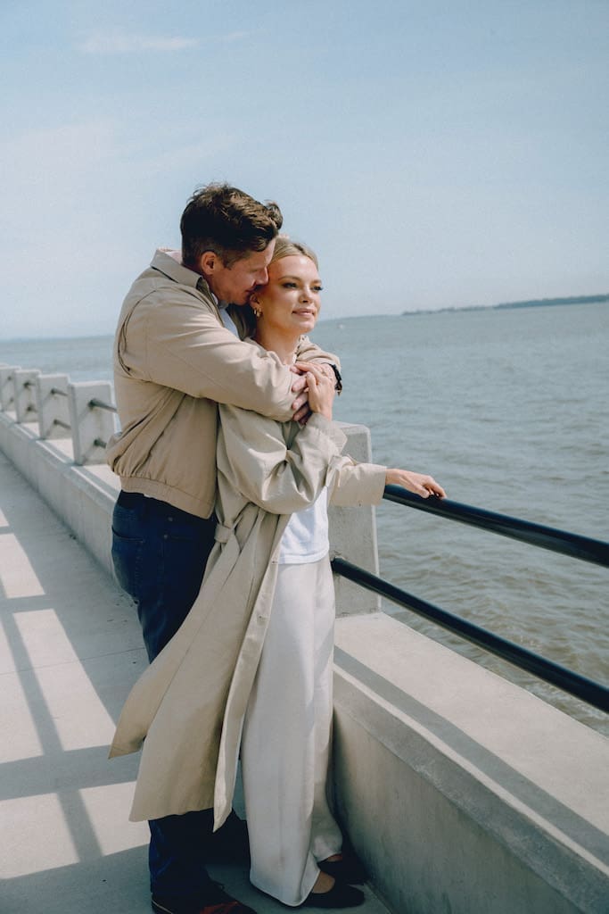 couple holding hands together at battery park in front of the water in tan trench coat