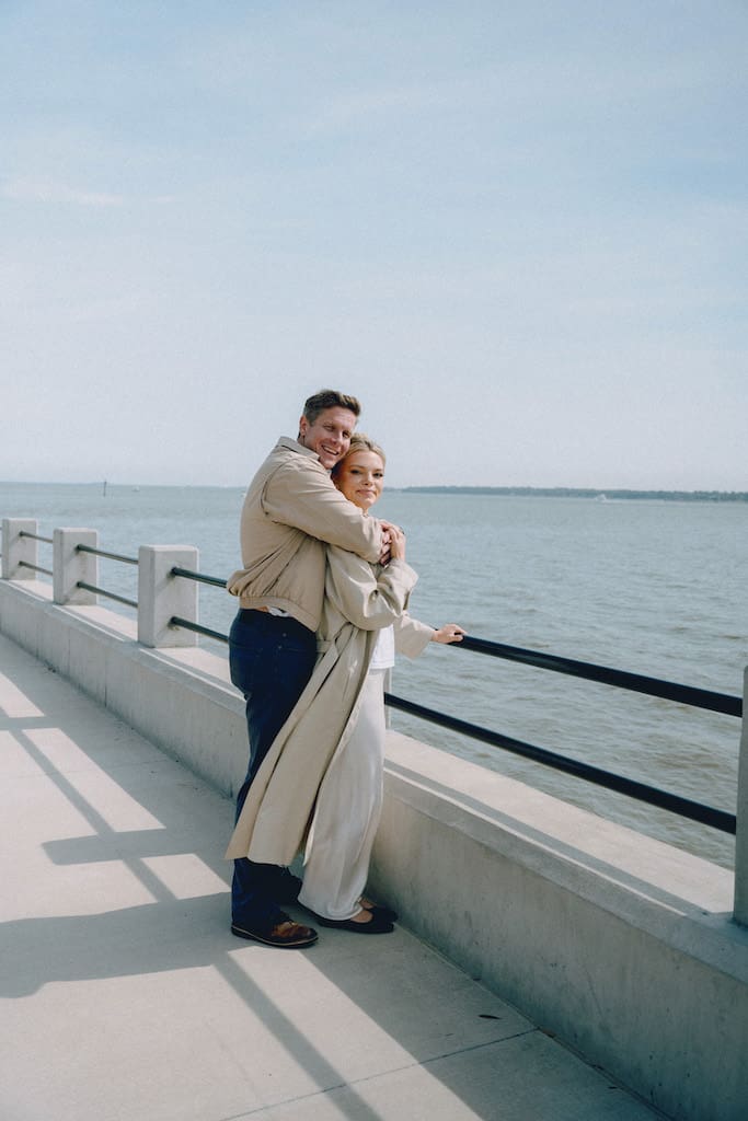 couple holding hands together at battery park in front of the water in tan trench coat