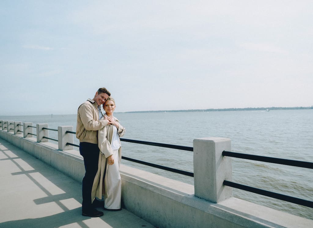 couple holding hands together at battery park in front of the water in tan trench coat