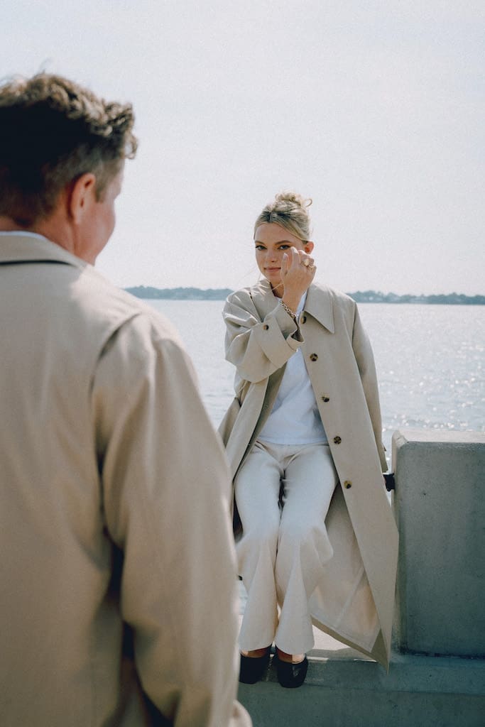 portrait of couple where she is looking at camera over mans shoulder with water in background