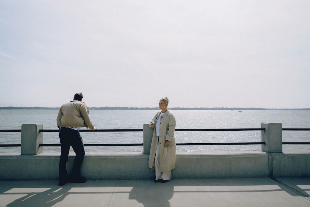 cinematic style photo of couple at battery park in front of water and railing, blue tones, true to life and moody 