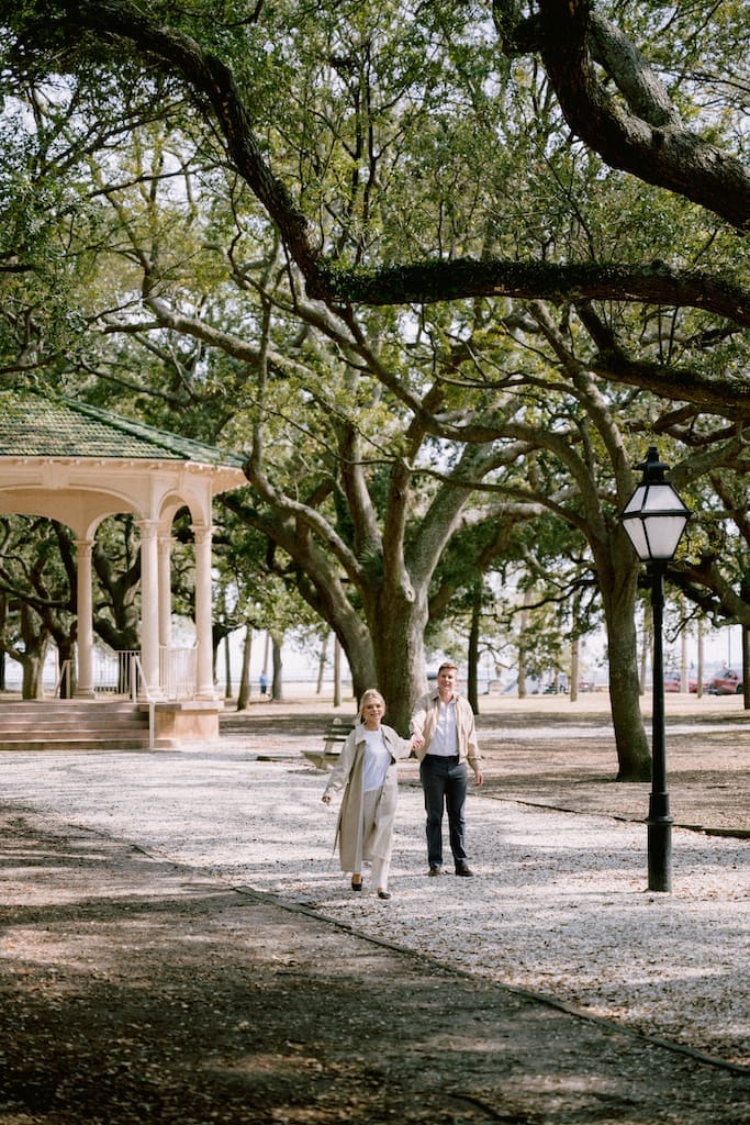 engagement photos in downtown charleston at white point gardens, couple walking together candidly in front of gazebo