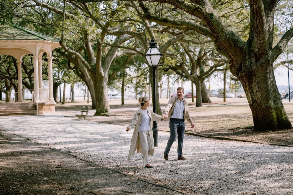 engagement photos in downtown charleston at white point gardens, couple walking together candidly in front of gazebo