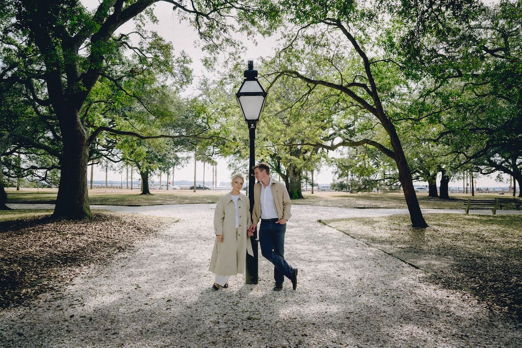 engagement shoot couple at battery park white point gardens leaning on lamp post in park in trench coats, fall and winter