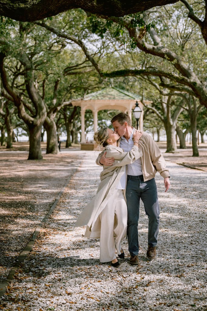 engagement photos in downtown charleston at white point gardens, couple walking together and kissing candidly in front of gazebo