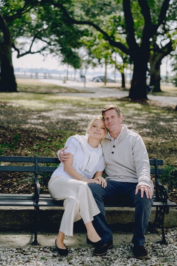 portrait of couple for engagement shoot at the battery in downtown charleston sitting on park bench under trees