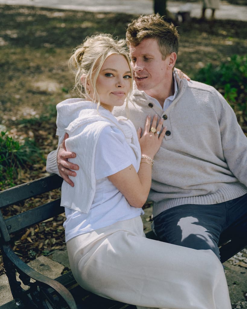 portrait of couple for engagement shoot at the battery in downtown charleston sitting on park bench under trees