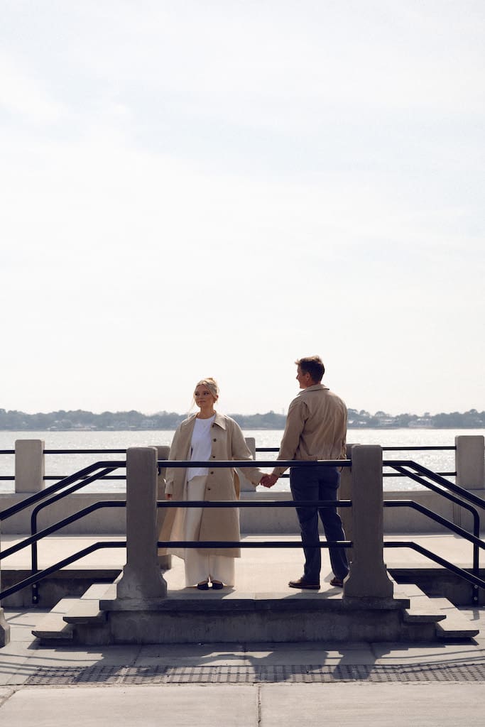 couple holding hands together at battery park in front of the water in tan trench coat