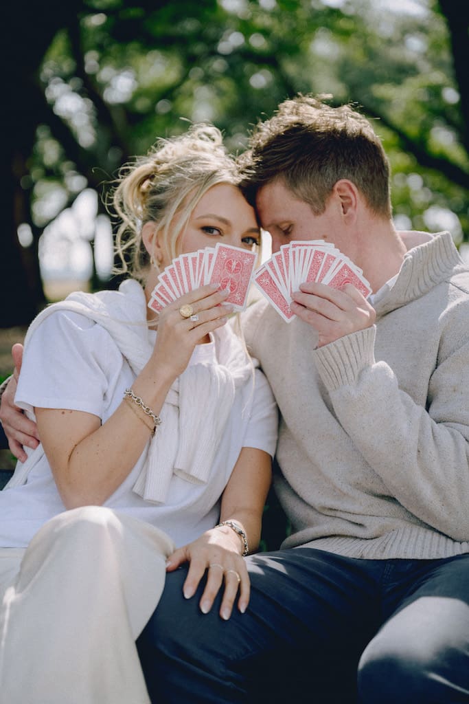 portrait of couple for engagement shoot at the battery in downtown charleston sitting on park bench under trees with cards
