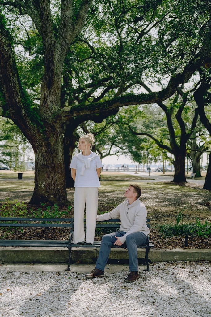 portrait of couple for engagement shoot at the battery in downtown charleston sitting on park bench under trees