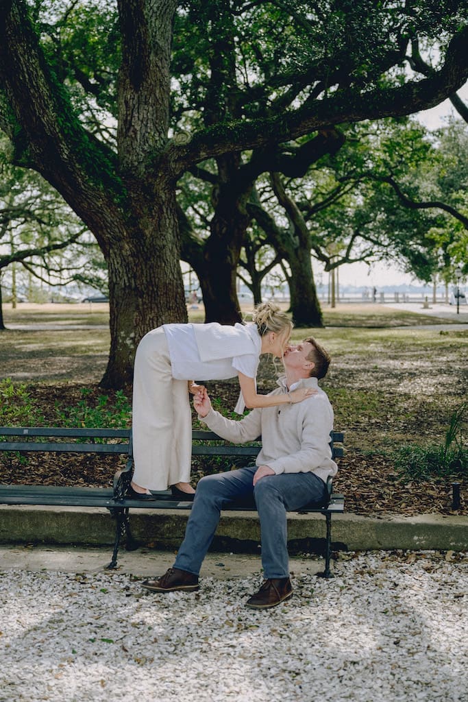 portrait of couple for engagement shoot at the battery in downtown charleston sitting on park bench under trees