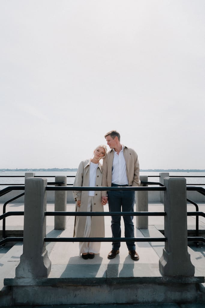 couple holding hands together at battery park in front of the water in tan trench coat