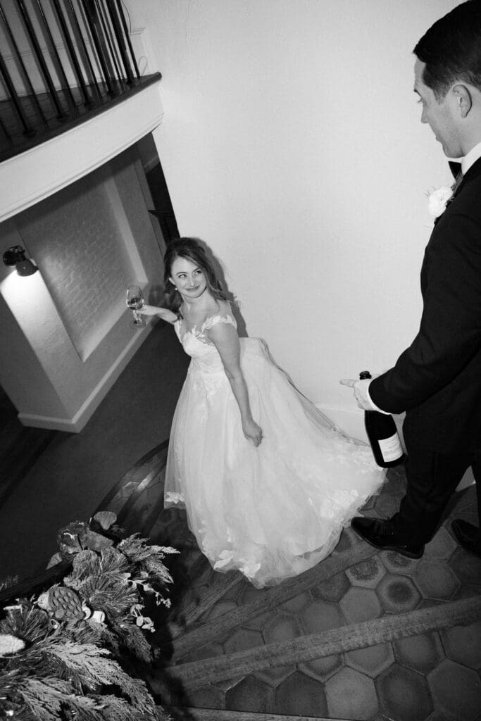 black and white photo of couple walking down the stairs on wedding day with drinks at shepherds inn rhode island