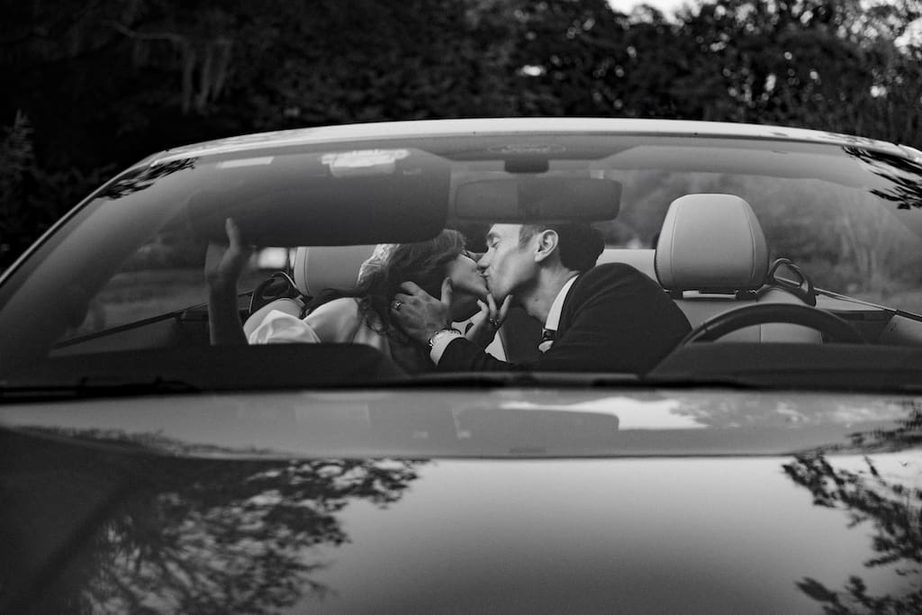 black and white photo of couple, bride and groom kissing in car shot through the window