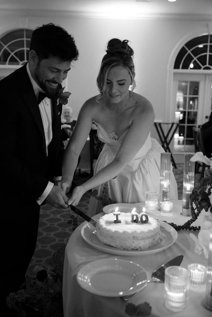 black and white photo of couple cutting wedding cake with candles dark and moody