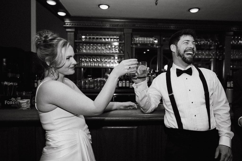black and white candid photo of couple cheersing at the bar during reception on wedding day
