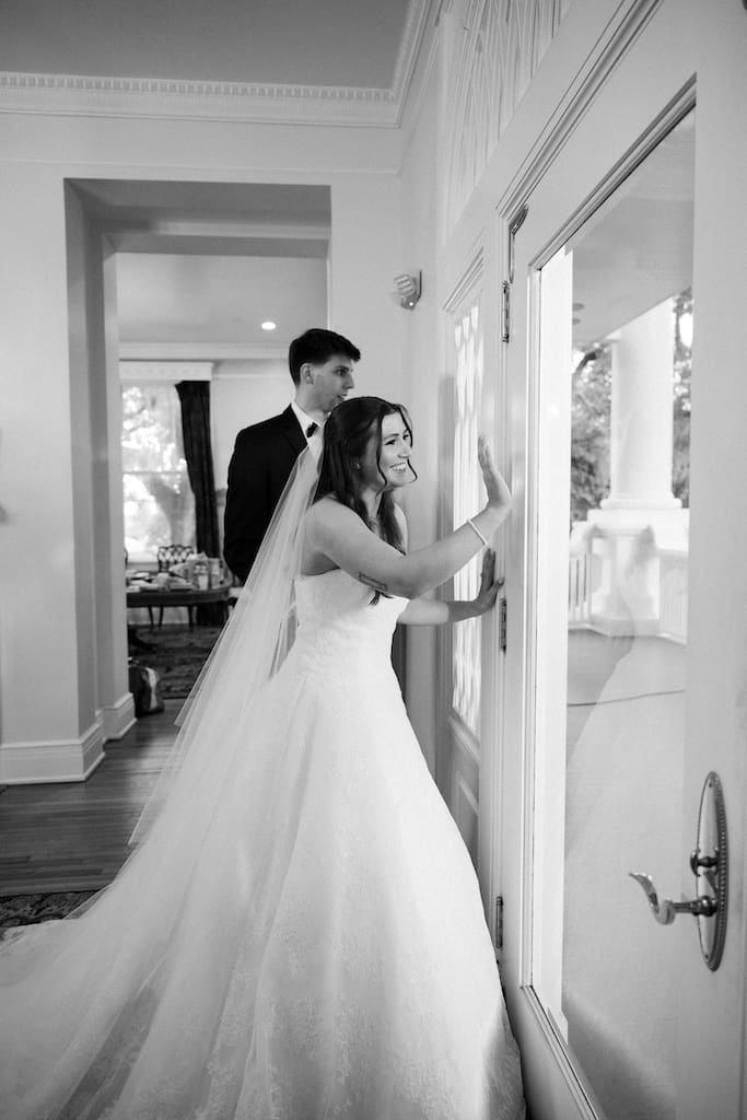 black and white photo of bride waving to guests out of a window